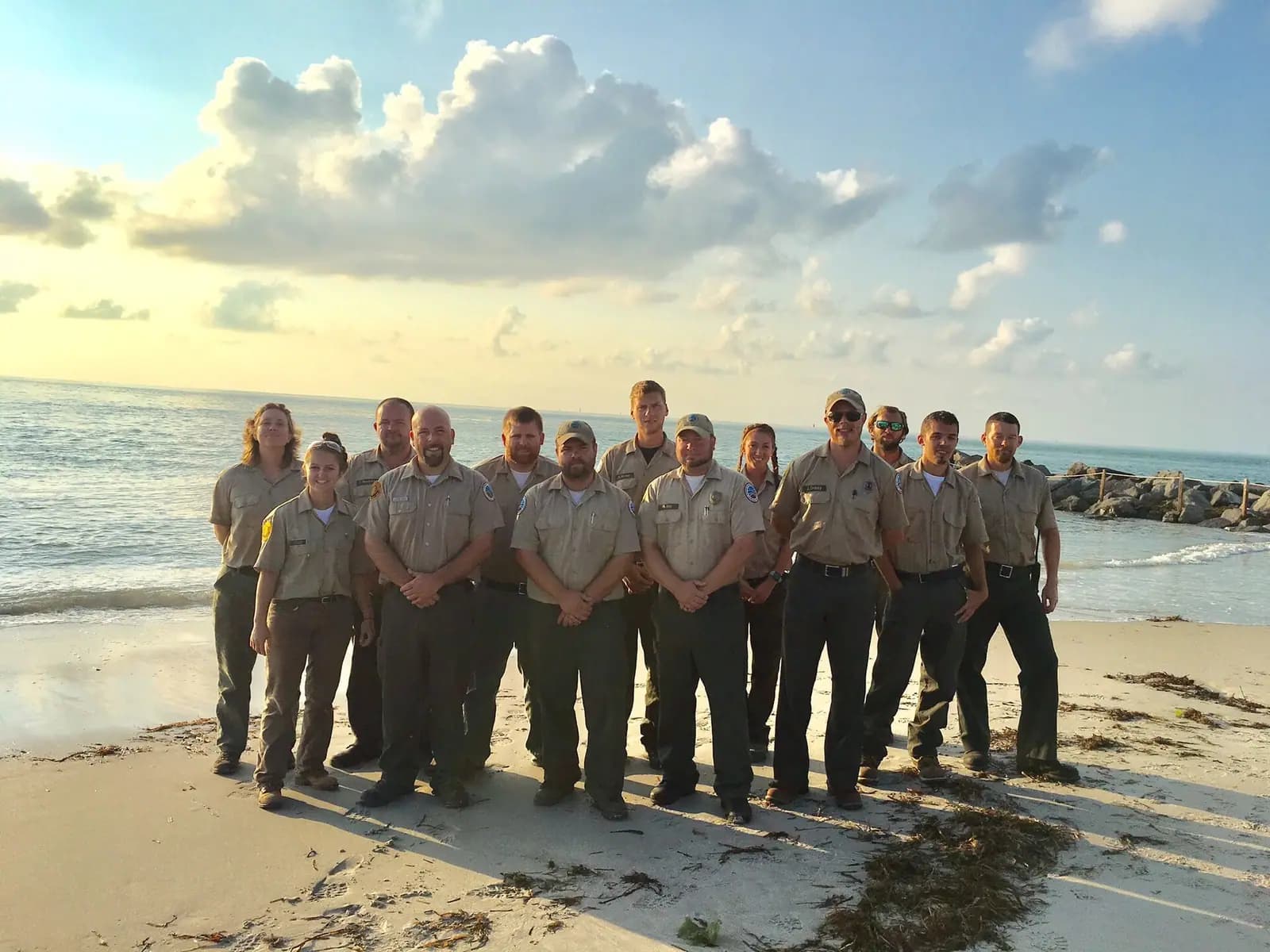 A tall white brick lighthouse standing above low coastal scrub against a clear sky