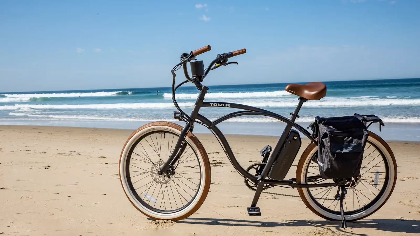 A bicycle with a pannier standing on sand beside breaking surf