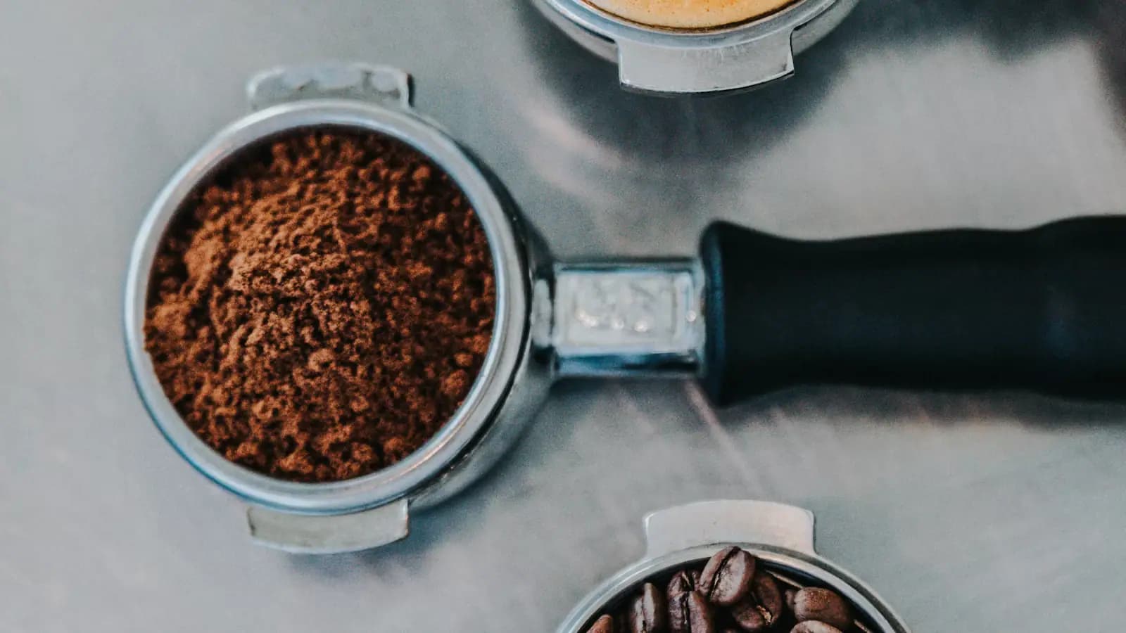 An espresso portafilter filled with freshly ground coffee on a metal counter