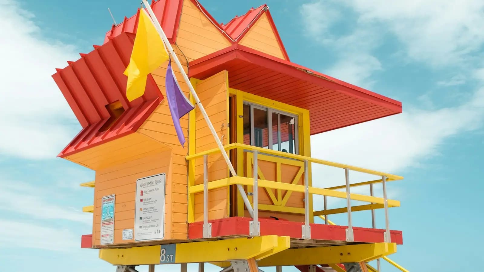 A brightly painted orange and red Miami Beach lifeguard stand flying yellow and purple warning flags