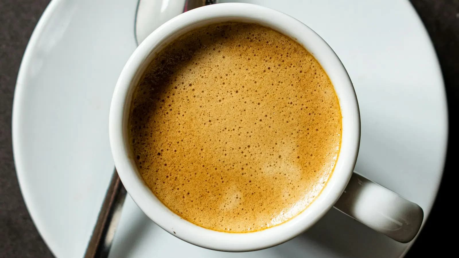 A small cup of strong black coffee on a saucer with a spoon beside it