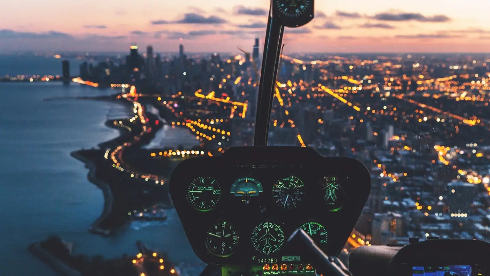The view forward from a helicopter cockpit over a waterfront city and open water