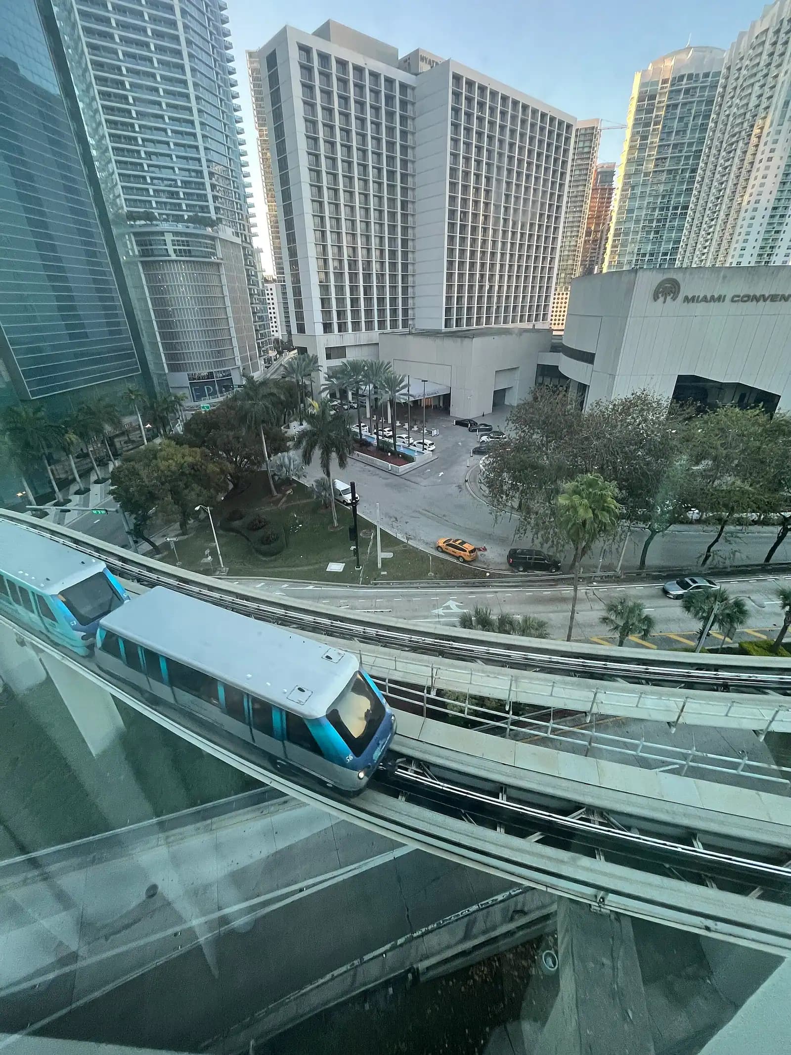 A small elevated train running on a raised concrete guideway between city office towers