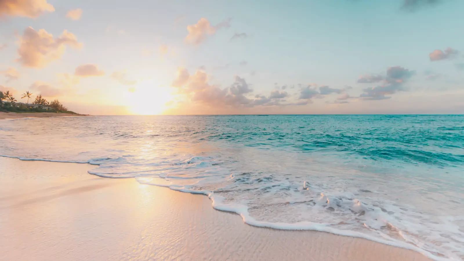 Gentle surf running onto pale sand at sunrise with a turquoise sea beyond