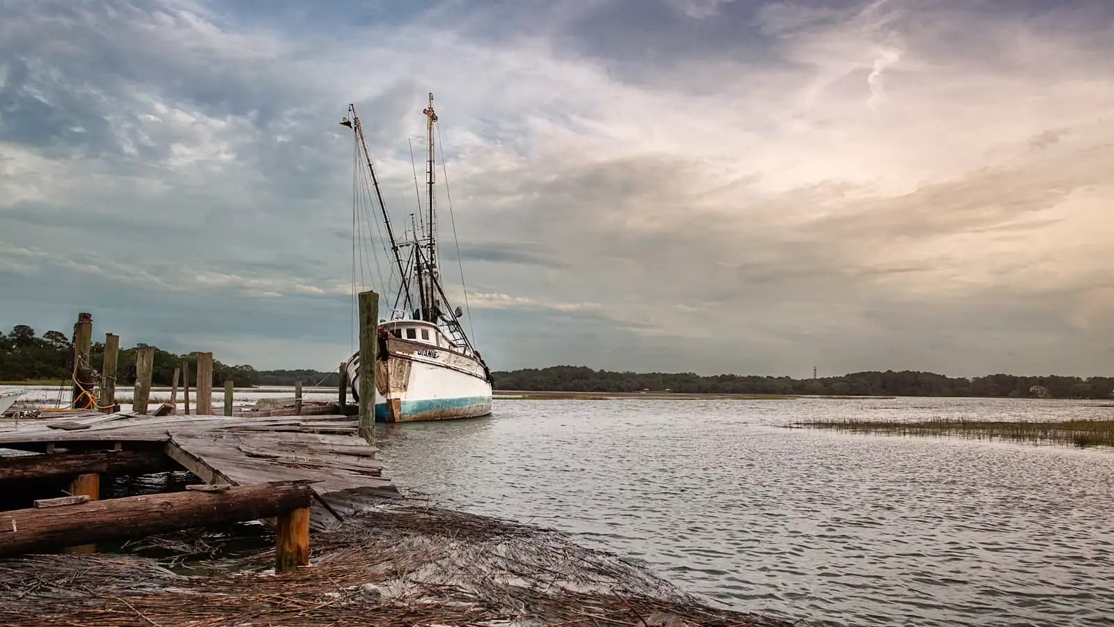 A working fishing boat tied up at a weathered timber dock under a heavy sky