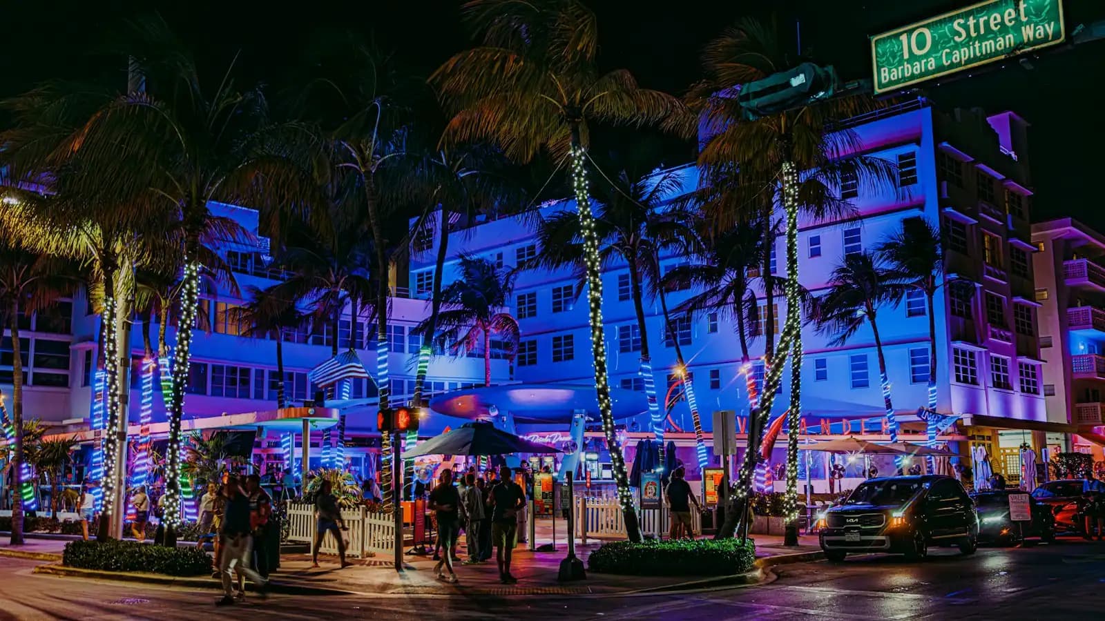 A city street after dark with neon-lit building frontages and palm trees