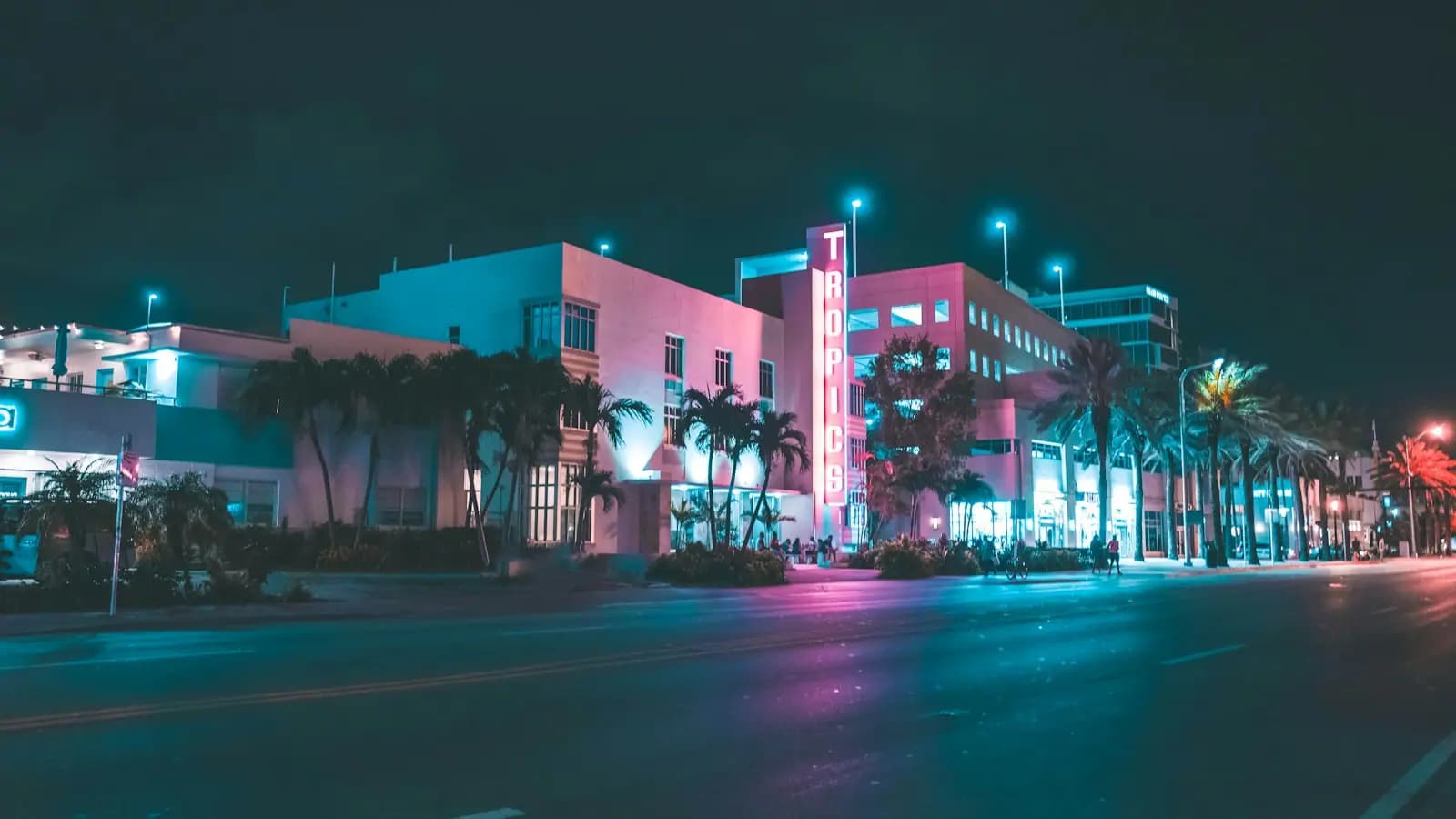 A neon-lit Art Deco hotel on a palm-lined Miami Beach street at night