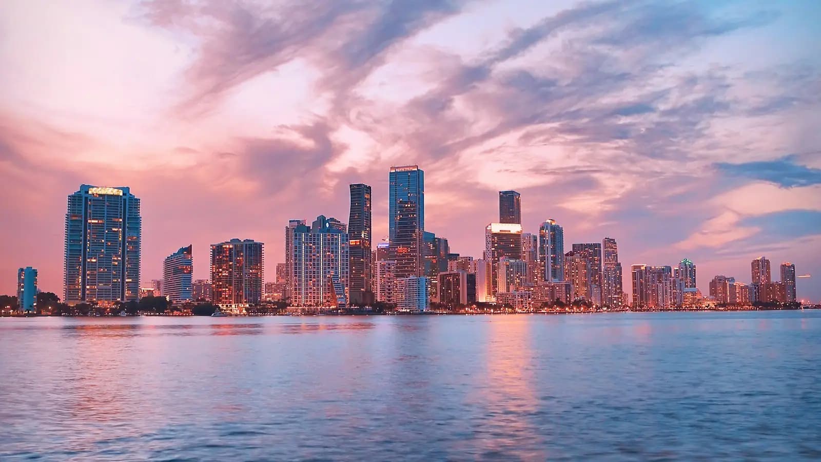 The Miami skyline at dusk seen across Biscayne Bay under a pink and violet sky