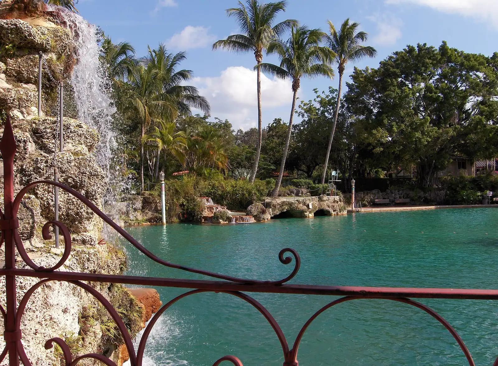 A large outdoor swimming pool with exposed limestone rock walls, palms and a stone bridge